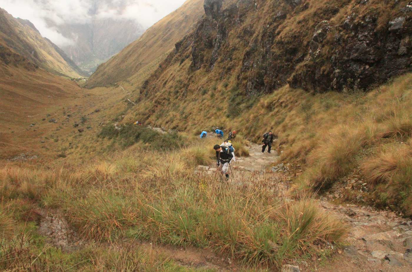Trekkers climbing a stone staircase through a high Andean valley on the Inca Trail
