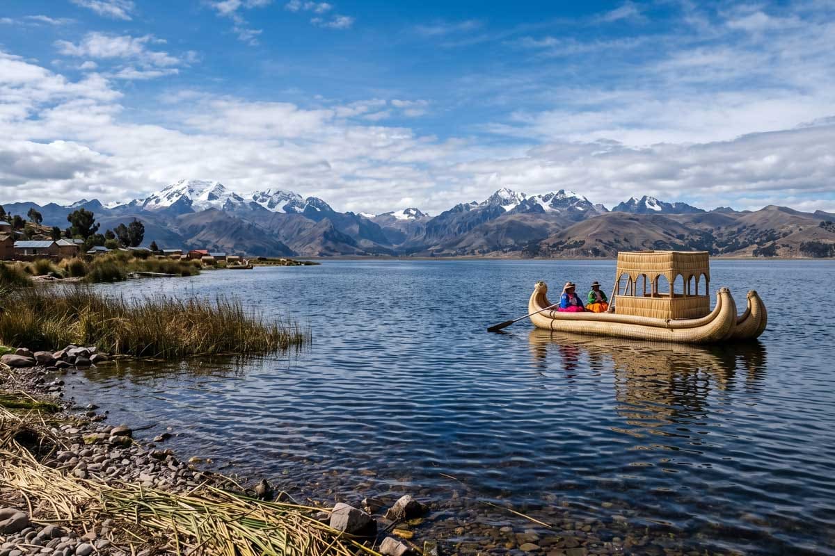 Traditional totora reed boat with passengers on Lake Titicaca, snow-capped Cordillera Real behind