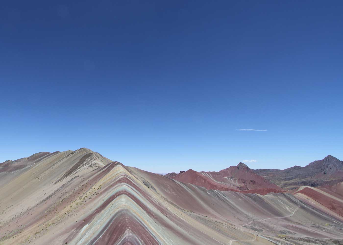 The striped red, tan, and white mineral bands of Vinicunca (Rainbow Mountain) under a clear sky