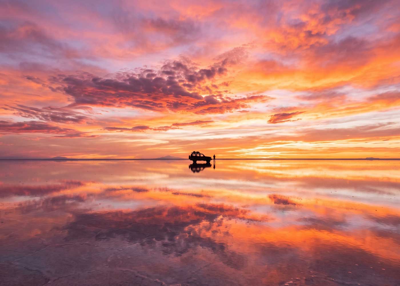 Vehicle silhouetted against a mirrored sunset reflection on the Uyuni salt flats