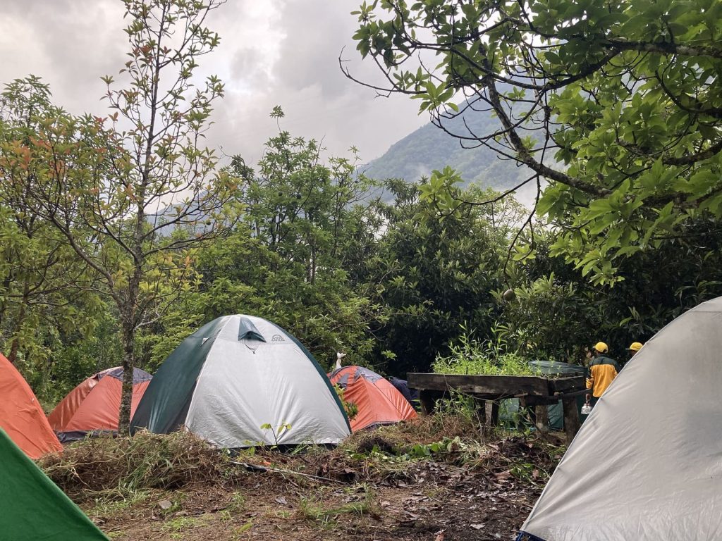 Tents at an Inca Trail campsite at dawn, with porters in yellow packing up camp