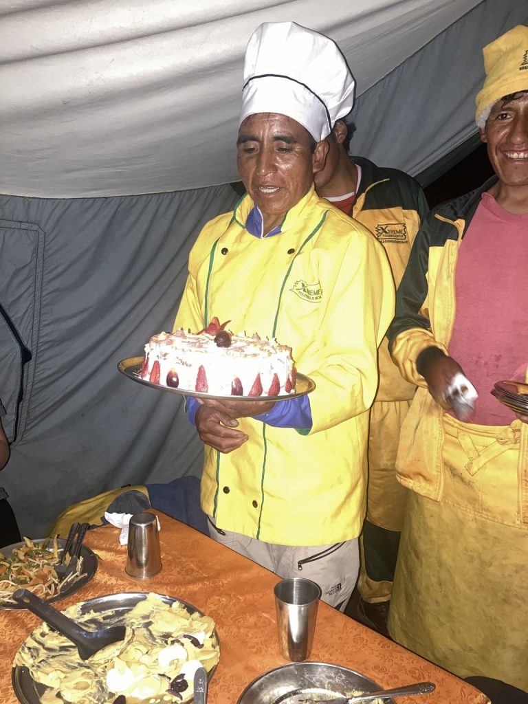 Two Inca Trail cooks in yellow jackets holding a cake in the dining tent