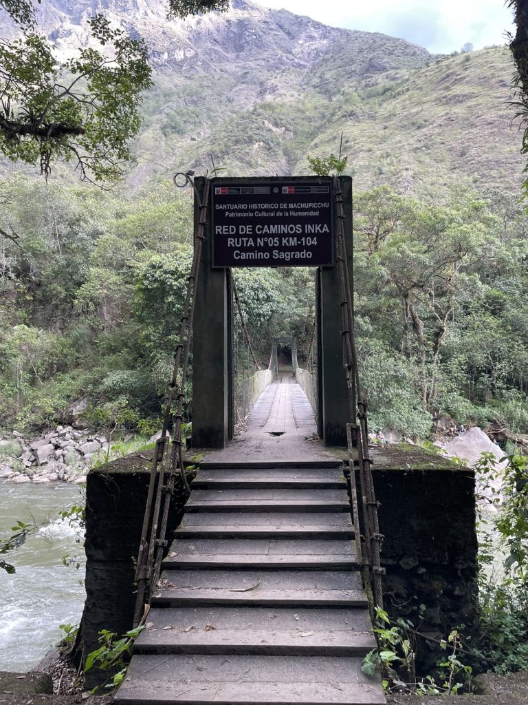 Suspension bridge over the Urubamba River at Km 104, with a sign reading Red de Caminos Inka, Ruta 05 KM-104, Camino Sagrado