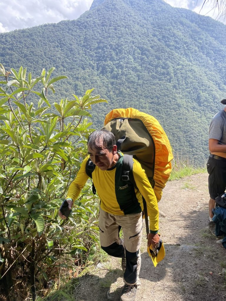 Inca Trail porter in a yellow uniform carrying a load up the trail