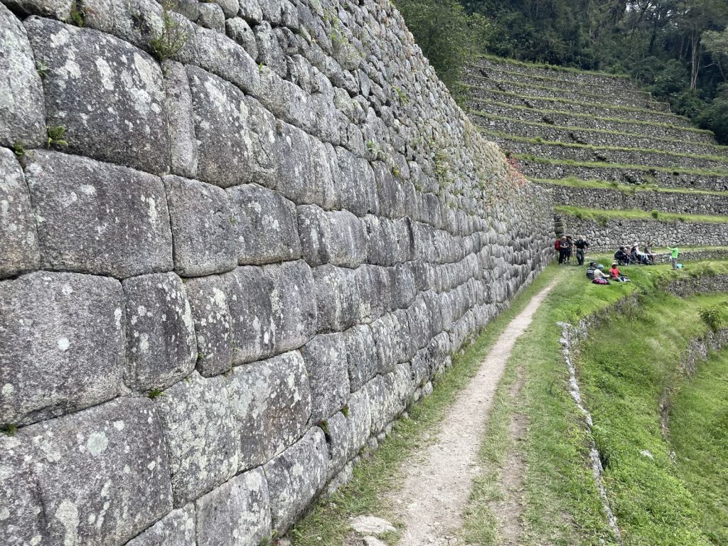 A narrow earth trail running beside a tall Inca stone wall and green terraces
