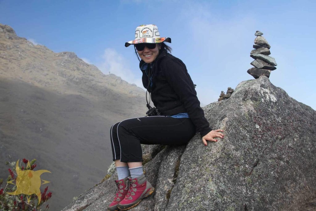 A trekker resting beside a stone apacheta cairn on a high Andean pass
