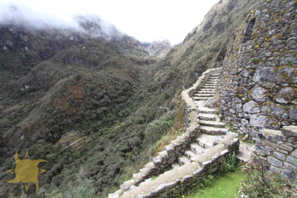 A curving Inca staircase beside a terraced retaining wall above a cloud-forest valley